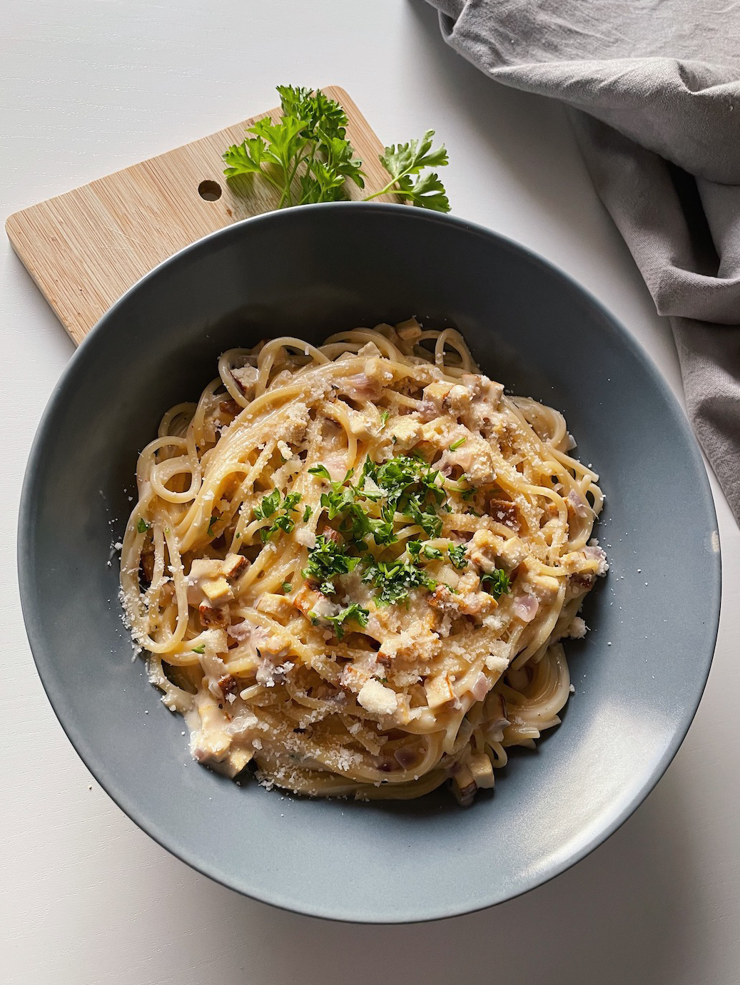 Teller mit leckerer veganer Spaghetti Carbonara, angerichtet mit Käse und Petersilie